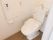 温水洗浄便座が採用されたトイレである。ボタンが便器の脇にあり、操作がしやすくなっている。壁にL字型の手すりがある。