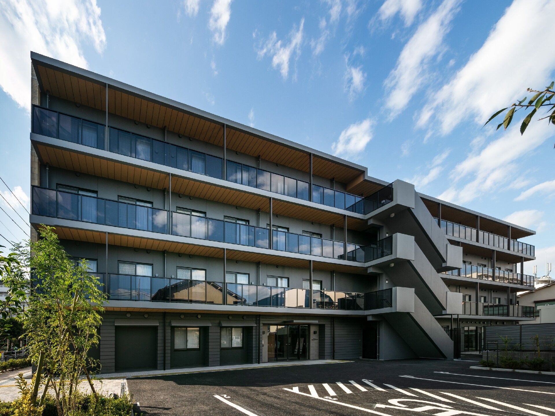 ベランダ付きの４階建ての建物。周囲には緑が多く大きな駐車場もある。