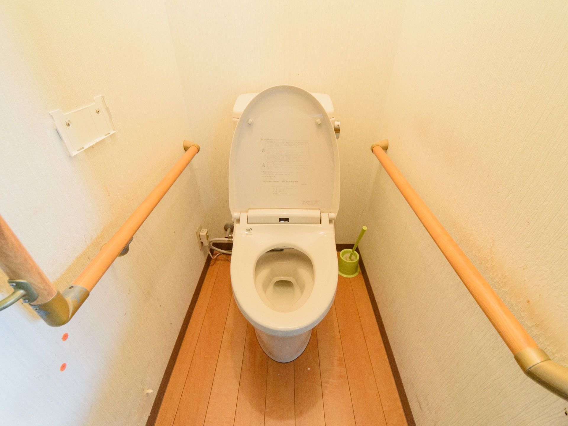 白を基調とした清潔なトイレである。両サイドの壁には手すりが取り付けられている。床には清掃用具が置かれている。