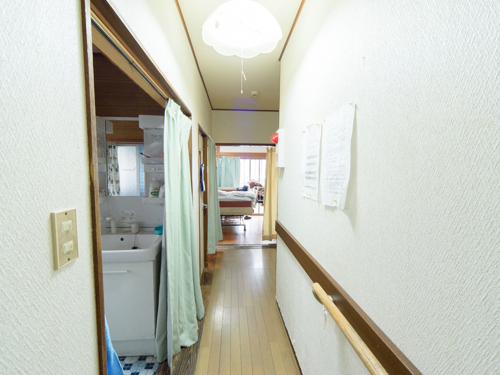 洗面所、共有スペースに繋がる通路である。床はフローリングが施されており、壁には手すりが取り付けられている。