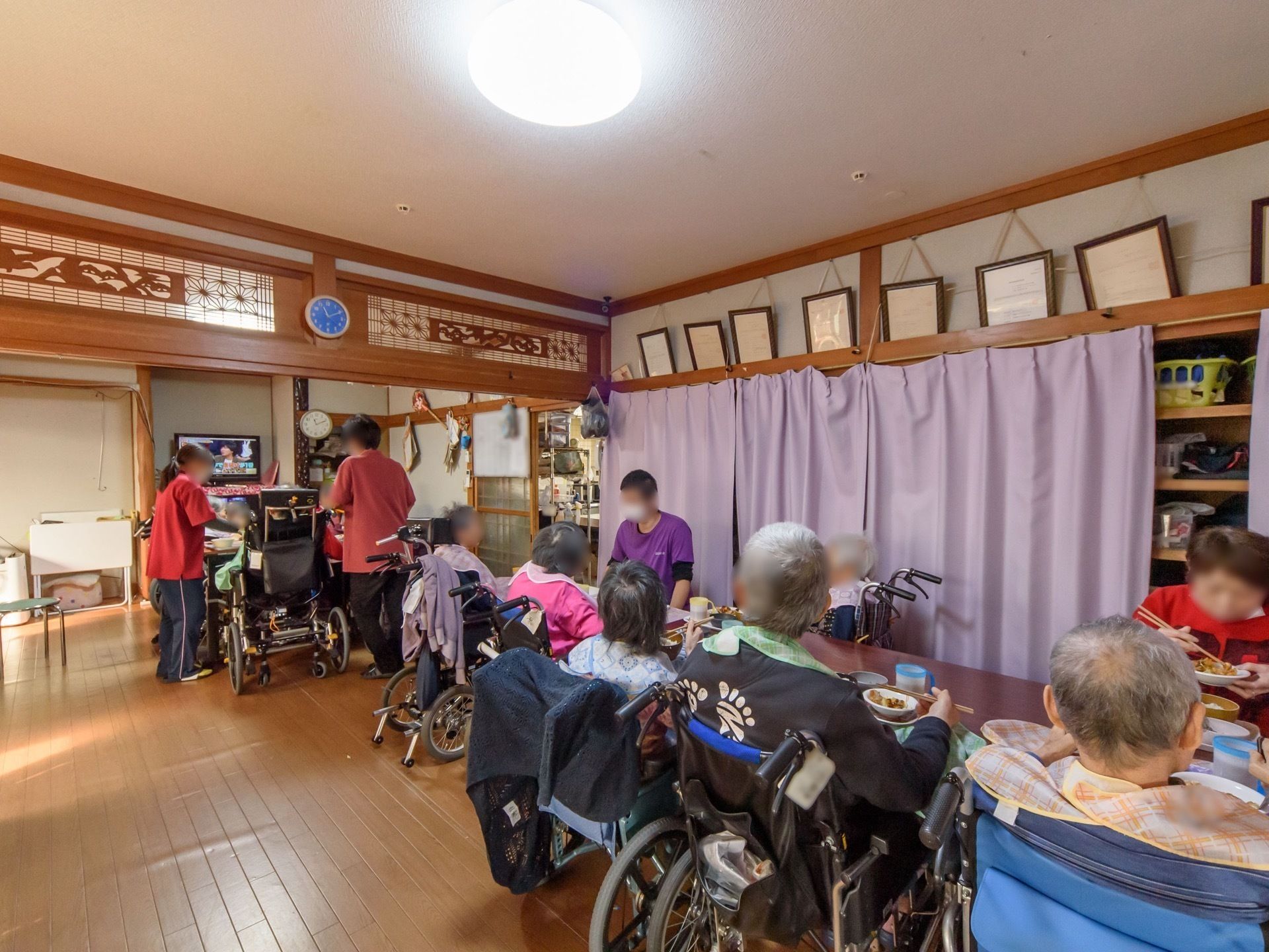 食堂のテーブルでテレビを見ながら、一緒に食事をする入居者の方々と、介助するスタッフ