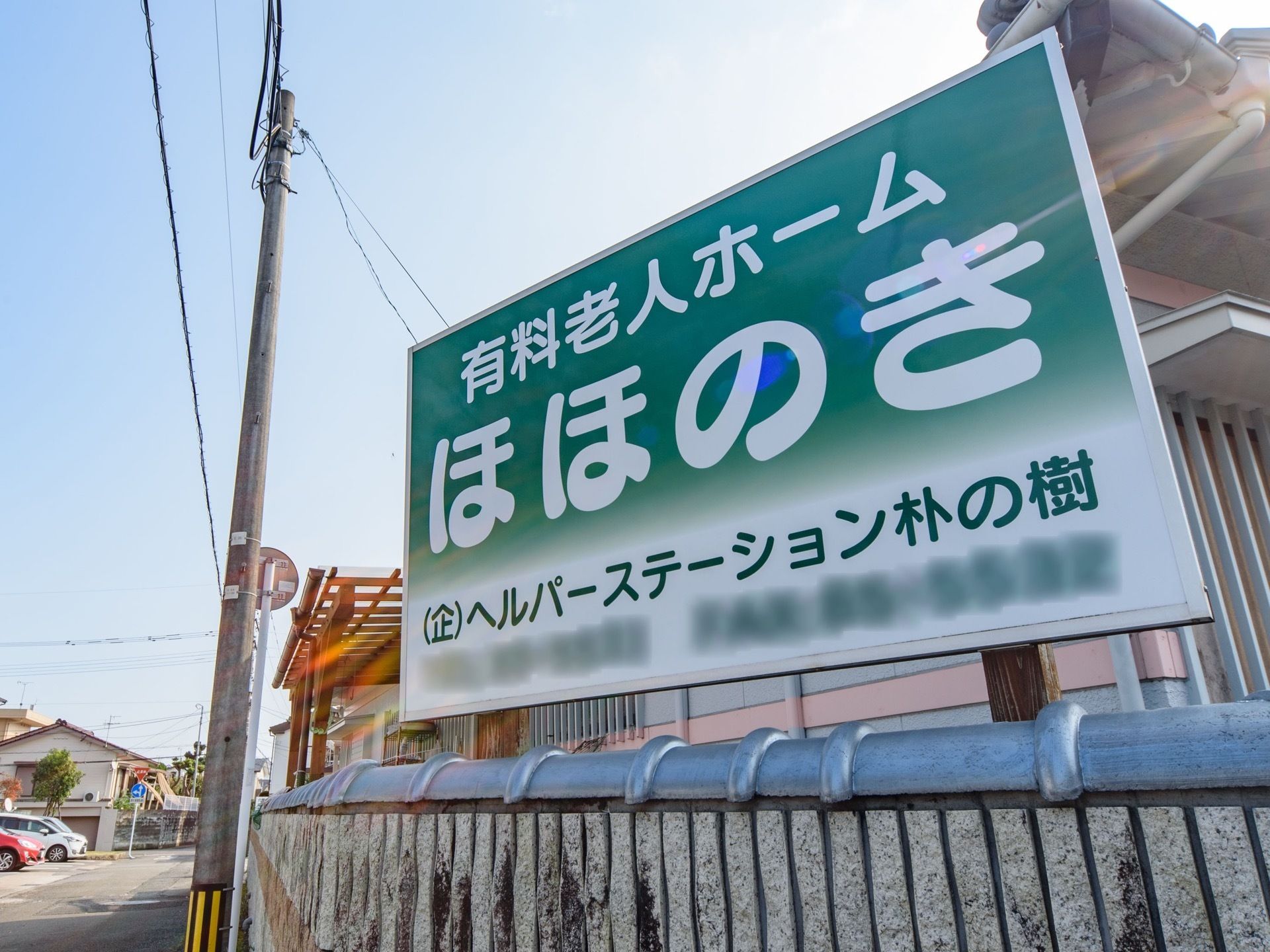 交差点から見やすい位置に、緑と白で描かれた看板が掲げられている。施設名の下には問い合わせ先が記されている。