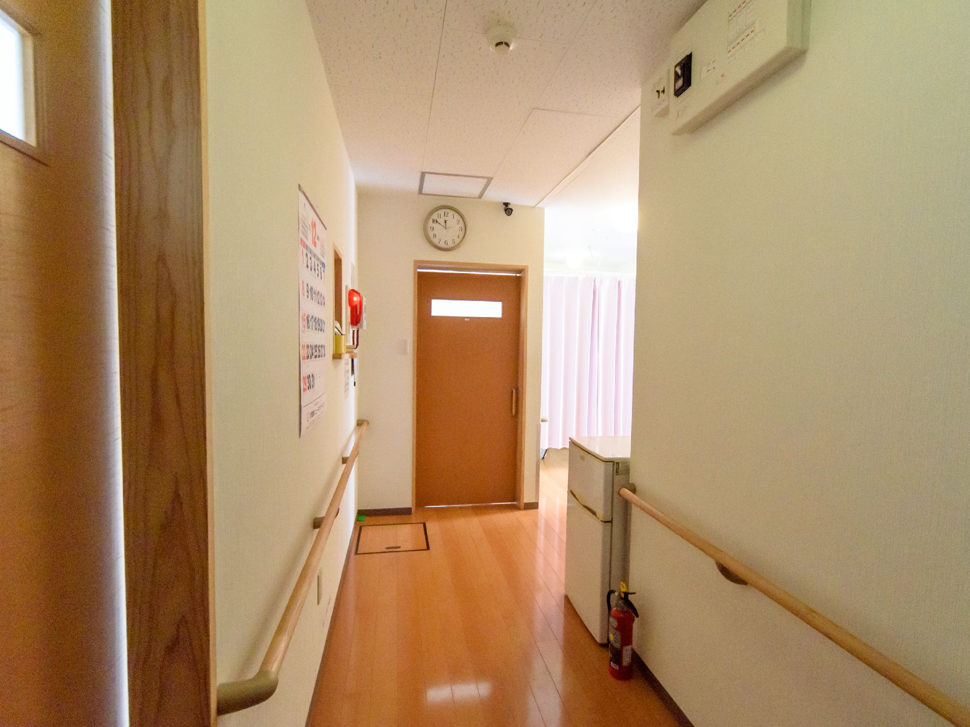天井にカメラが設置され、両側に手すりがあり、消火器と冷蔵庫が置かれた廊下