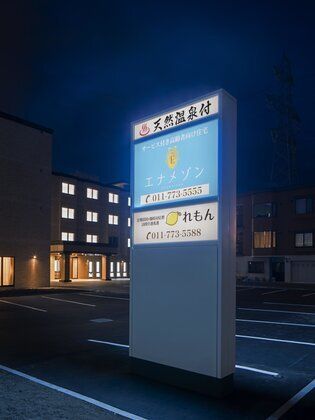 館銘板に明かりが点き、後ろには駐車場や建物があることがわかる。陽が沈み、暗くなった周辺。