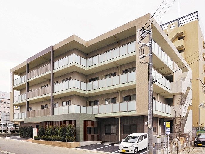 ベージュの建物は4階建てで、建物には屋外階段が付き、数台止める駐車スペースもある。