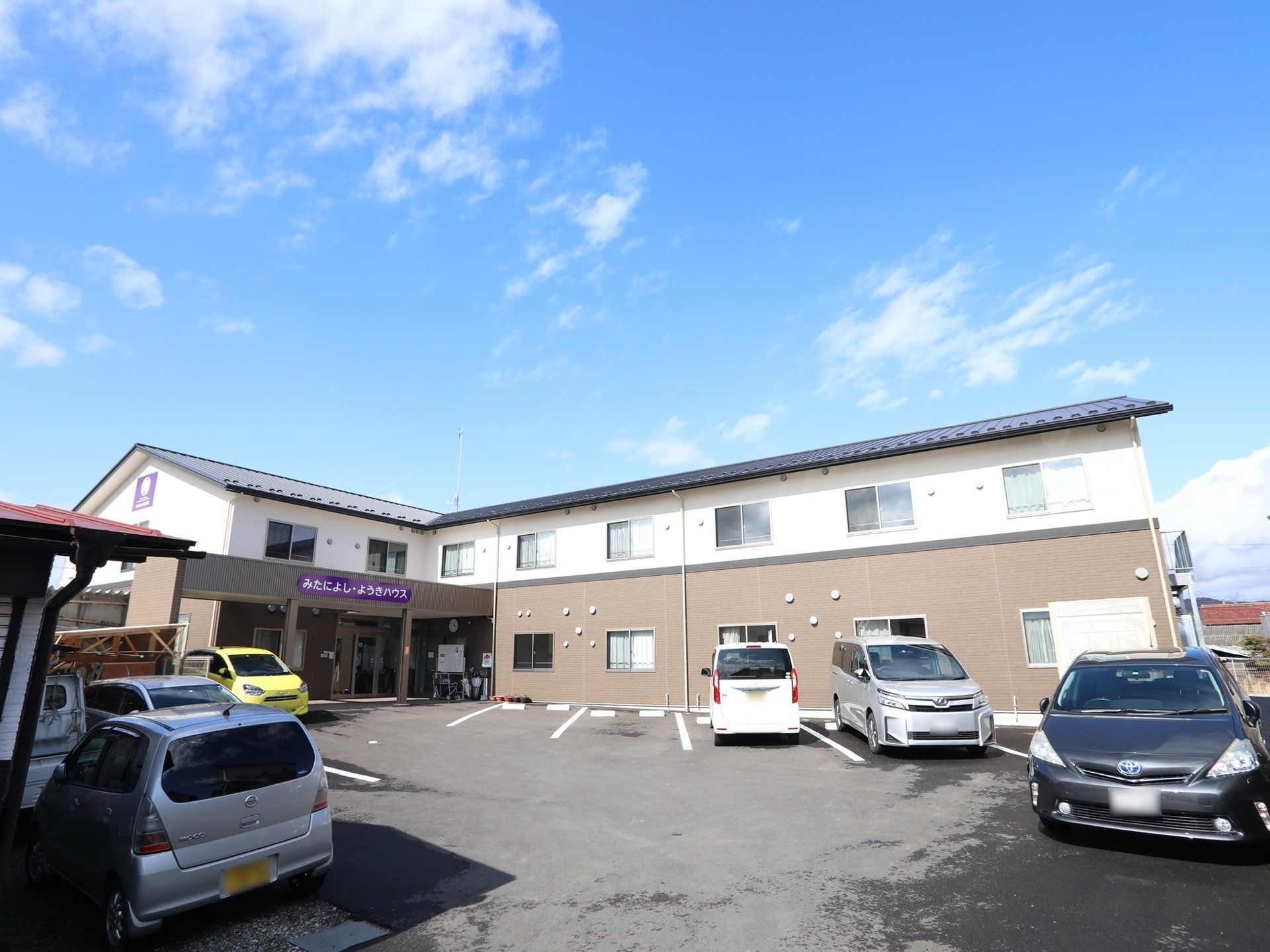 落ち着いた色合いの外観である。エントランスは屋根が付いている。側面には施設名が書かれた、看板が設置されている。