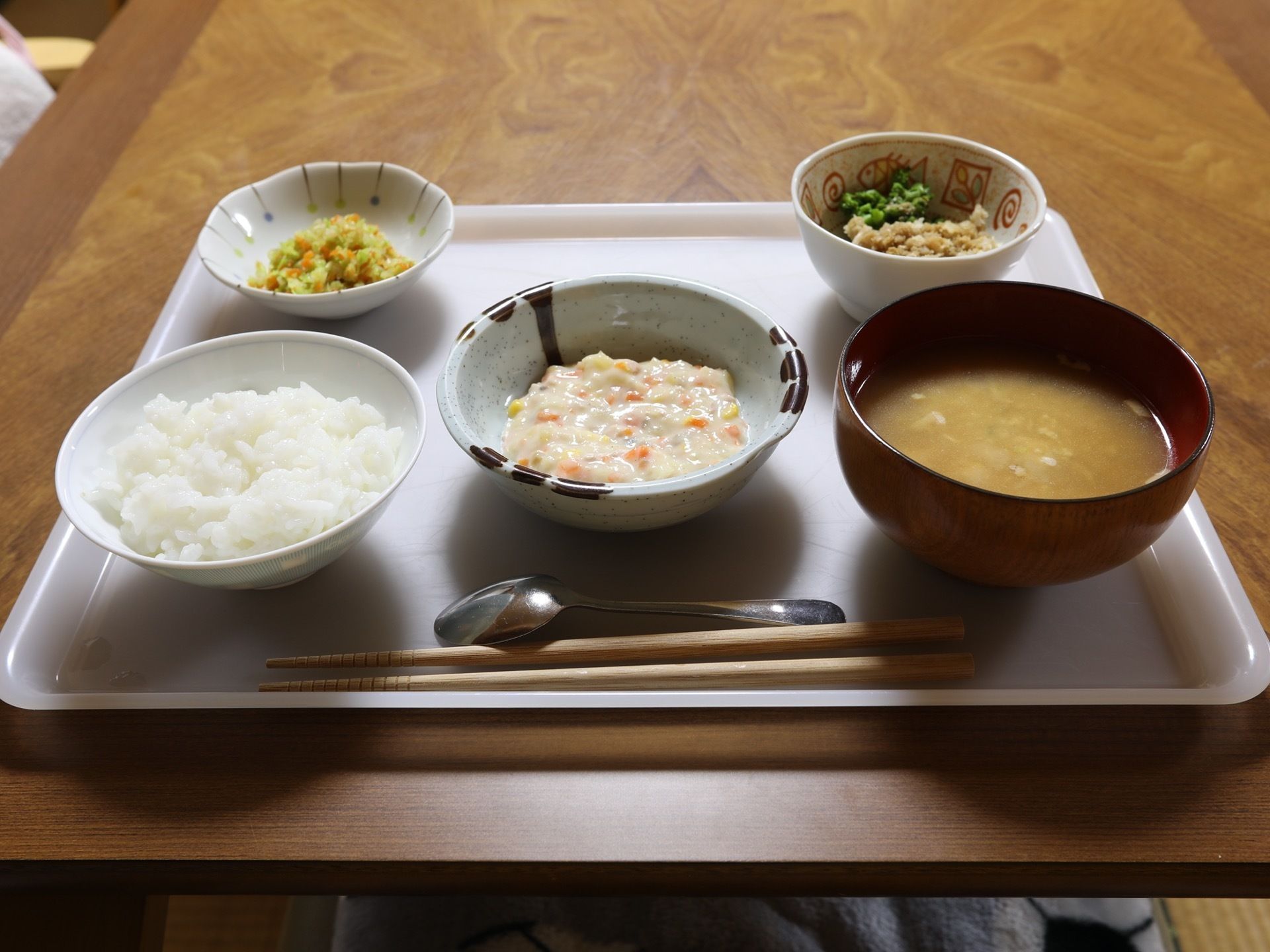 白色のトレーに、本日の料理がならべられている。白ご飯に主菜、汁物など品数が豊富である。スプーン、お箸も置かれている。