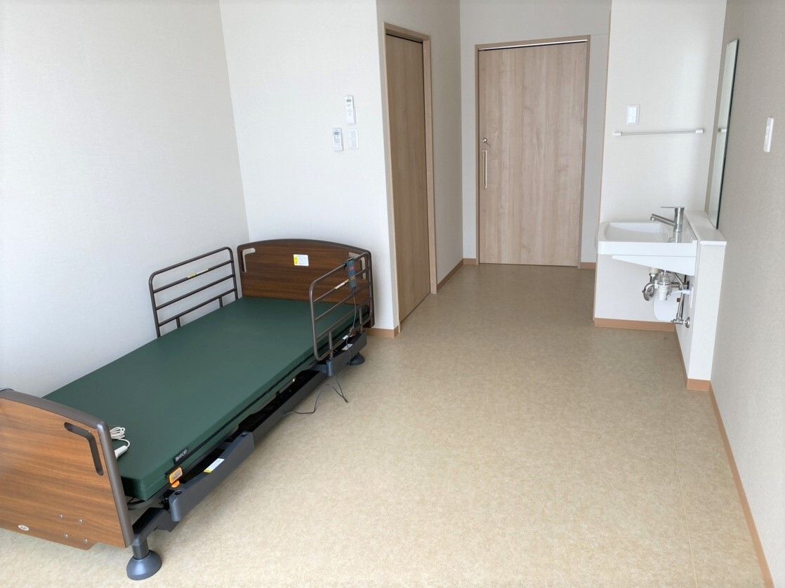 居室のドアが一番奥にあり、右手に洗面所、左手にトイレのドア、そして手前に介護ベッドが置かれている。