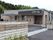 ブラウン系の平屋建ての建物の玄関には手すり付きのスロープが付き、自然に囲まれている。