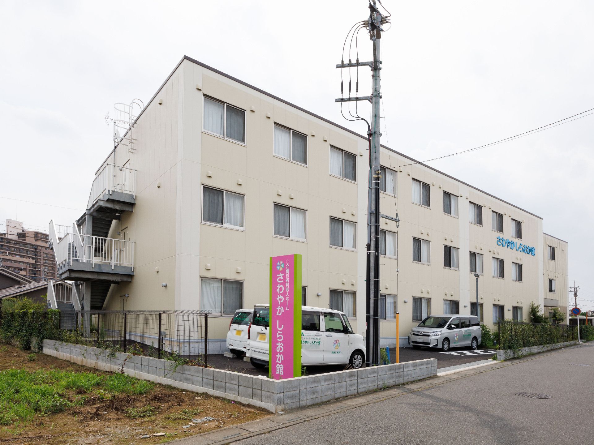 道路沿いに立地しているベージュ色の３階建ての建物