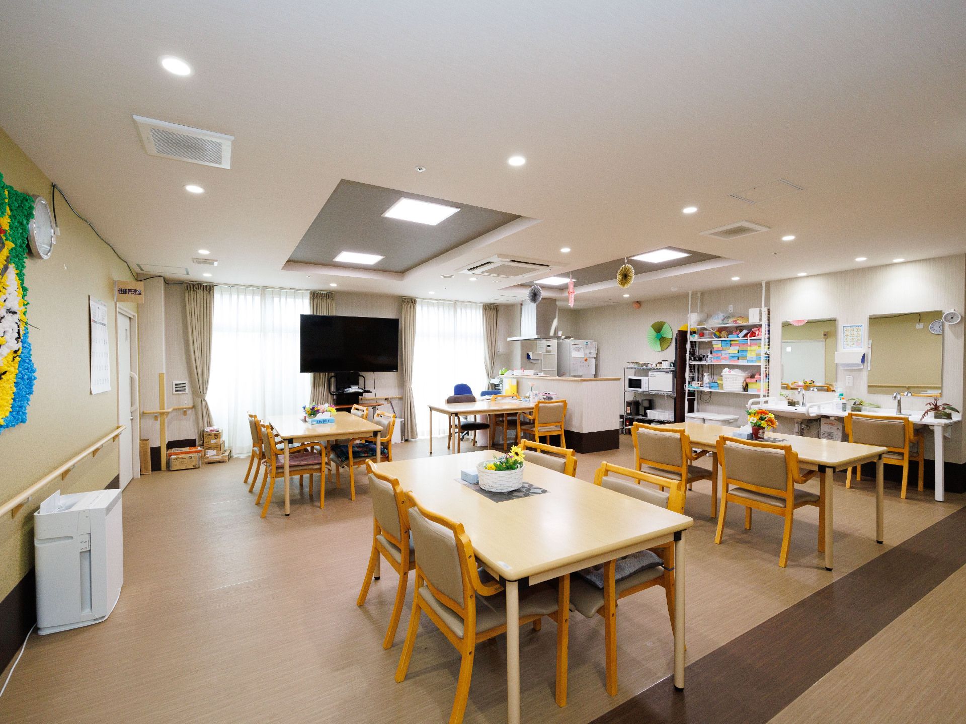 壁一面が窓ガラスの広間に並べられた木製の机と椅子