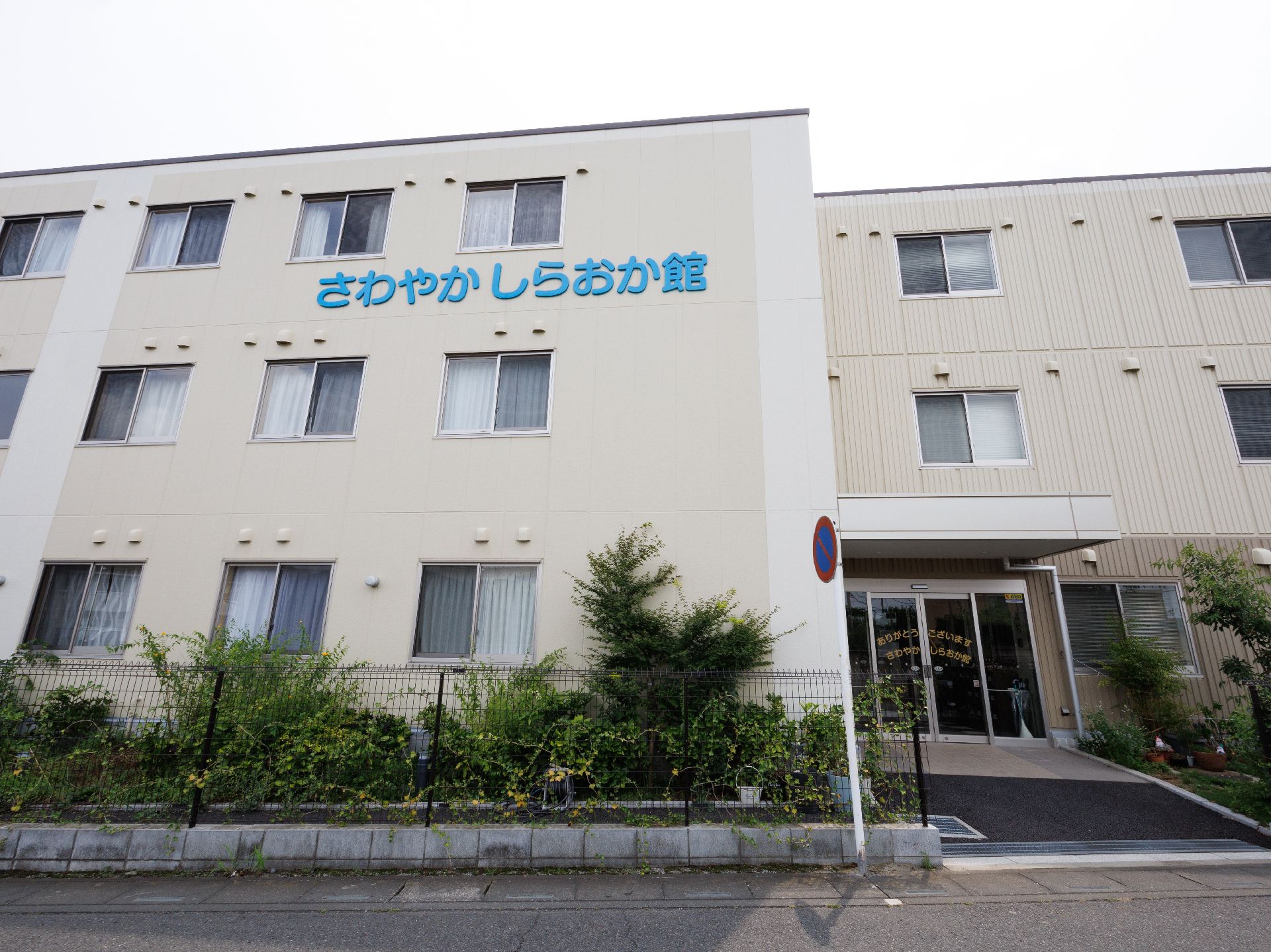 アスファルトの道路沿いに立地している３階建ての白い建物
