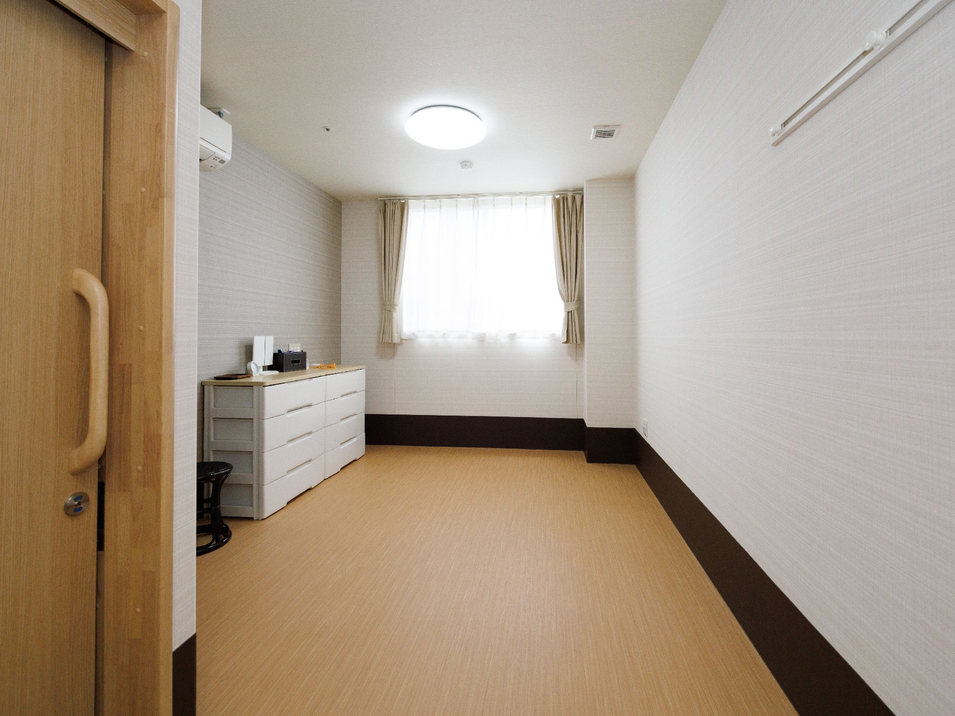 白い壁沿いに白い収納棚が置かれた窓が１つある部屋