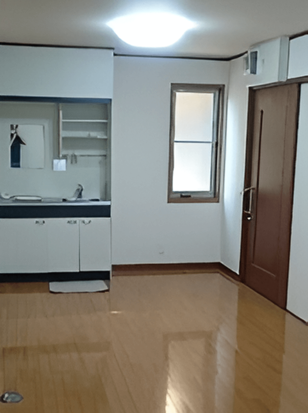 フローリングの部屋にはキッチンが付いている。大きなスライド式のドアが右側にあり、細長い窓がある。