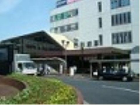 最寄り駅の建物の外観である。建物は４階建てで壁の色は白色系であり、駅前のロータリーの中央には緑の植物が植えられている。