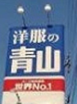 紳士服専門の衣料品店の看板である。店舗の屋上に掲げられ、青地に白色で店名が表示されている。看板には照明設備も設けられている。