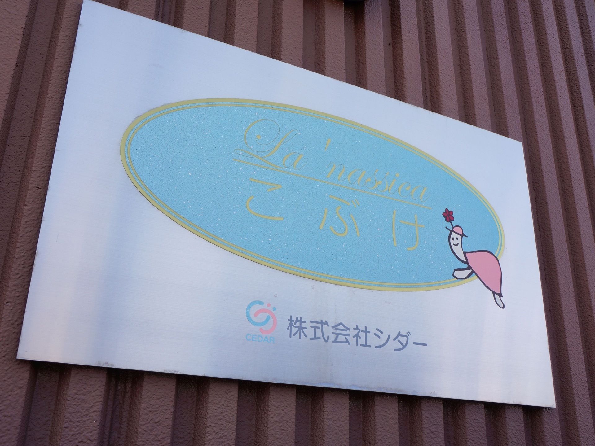 玄関ホールの右側に設置されている、施設のロゴマークの看板。シルバーの金属製の板に印刷されている。カメのマスコットが印象的である。