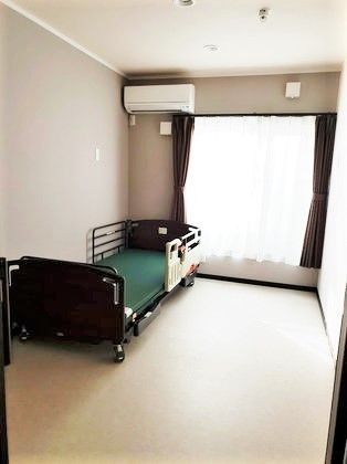 ベッドとエアコンが置いてある施設内の居室の様子。窓から非怒りが差し込んでいる