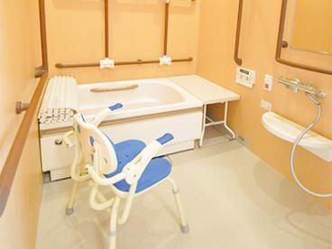 たくさんの手すりが設置され、呼び出しボタンやベンチが付いた一人用の浴槽が設置されている浴室。
