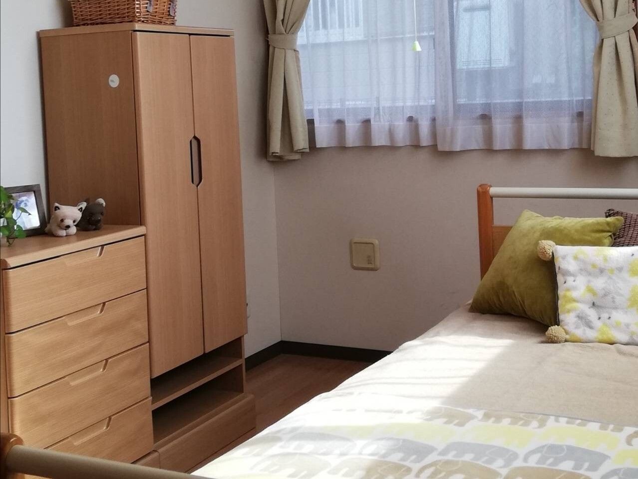 介護ベッドやタンスなどの家具が置かれたフローリングの部屋。ベッドサイドには緊急通報装置がある。
