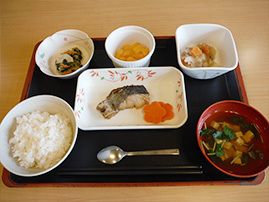 汁物や白いご飯、焼き魚に野菜の副菜が数種類並べられた黒いトレー。