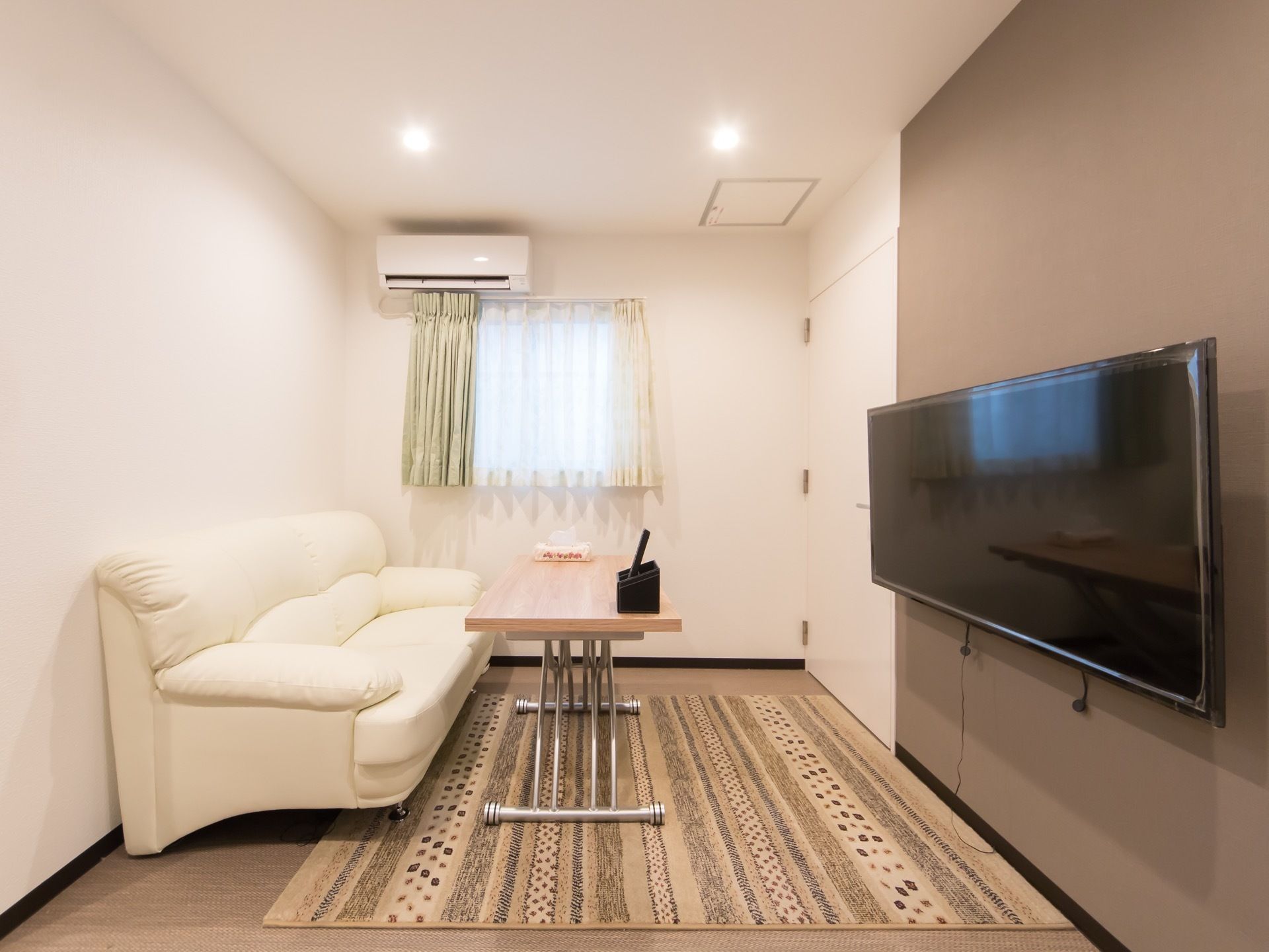 大きな白いソファとテーブルが置かれた共有スペース。壁にはエアコンや大型のテレビが備え付けられている。