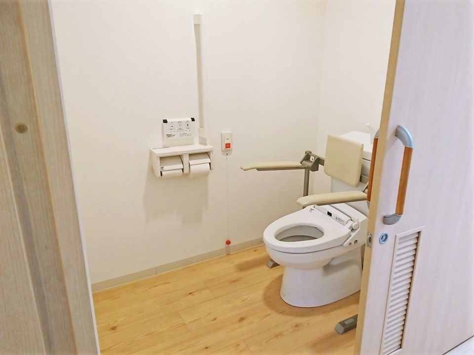 呼び出しボタンがついたトイレにはアイ字型の手すりがあり、便座にも手すりと背もたれが付き、フローリングで介助スペースも広い。