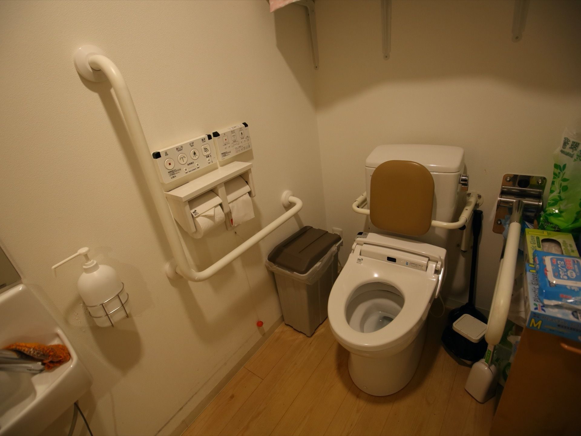 トイレは照明が内部を優しく照らしている。右側には備品が置かれており、反対側は水洗ボタンのほか手すりが設けられている。