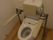 トイレの床はフローリングになっており、背もたれと手すりの付いた便器が設置されている。トイレのタンクの上には手洗い管が付いている。