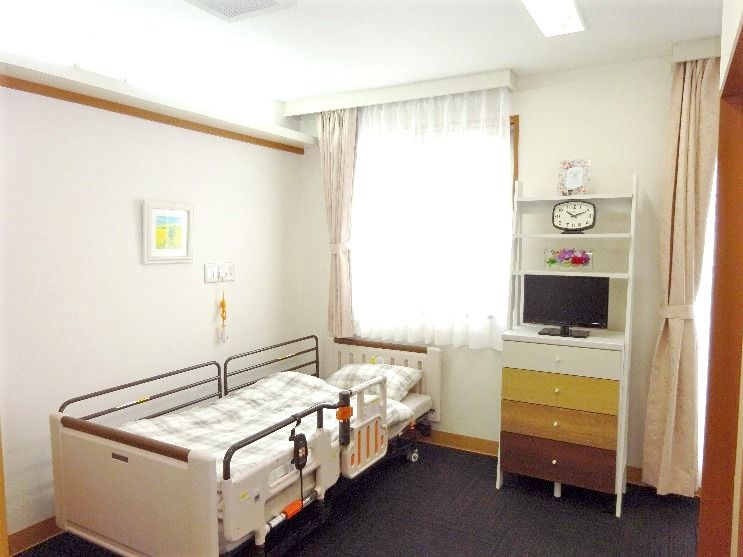 ベッドサイドには緊急通報装置が付いた個室の部屋には、介護用ベッドやテレビが置かれた収納家具などが置かれている。