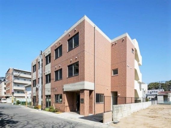 ブラウン系の3階建ての建物。各フロアにベランダが付き、周辺には住宅がたくさんある。