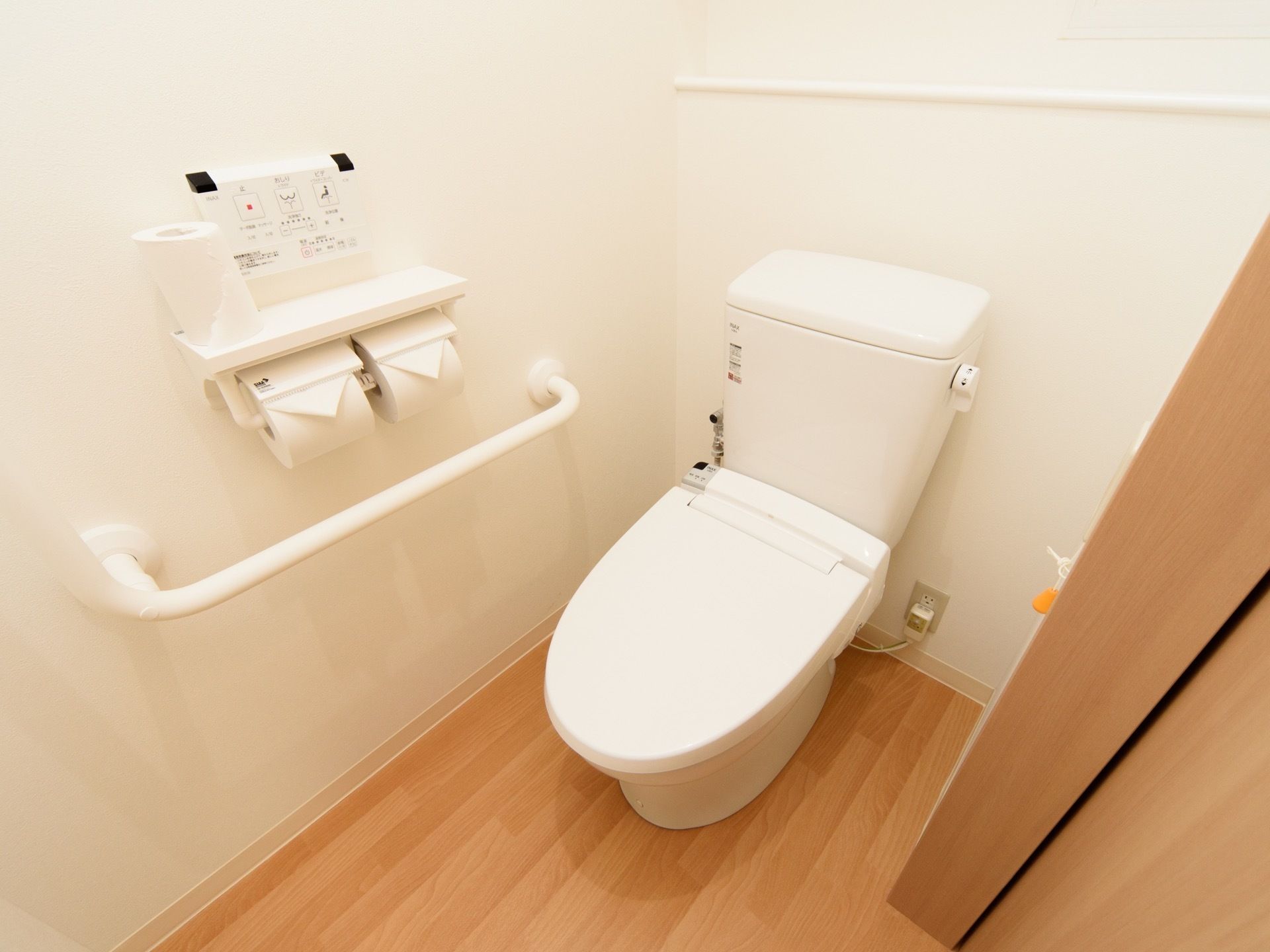 温水洗浄便座のついた、洋式便器を設置している。壁には操作パネルがあって、手すりがある。