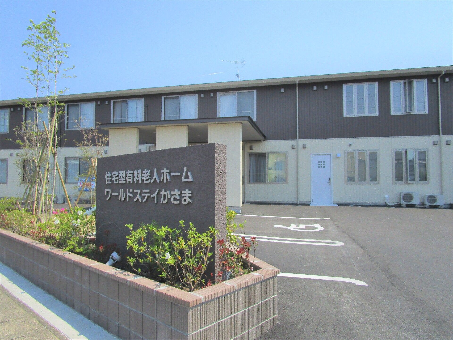 看板の後ろには広い駐車場が広がり、2階建てのモノトーンの建物が建っている。