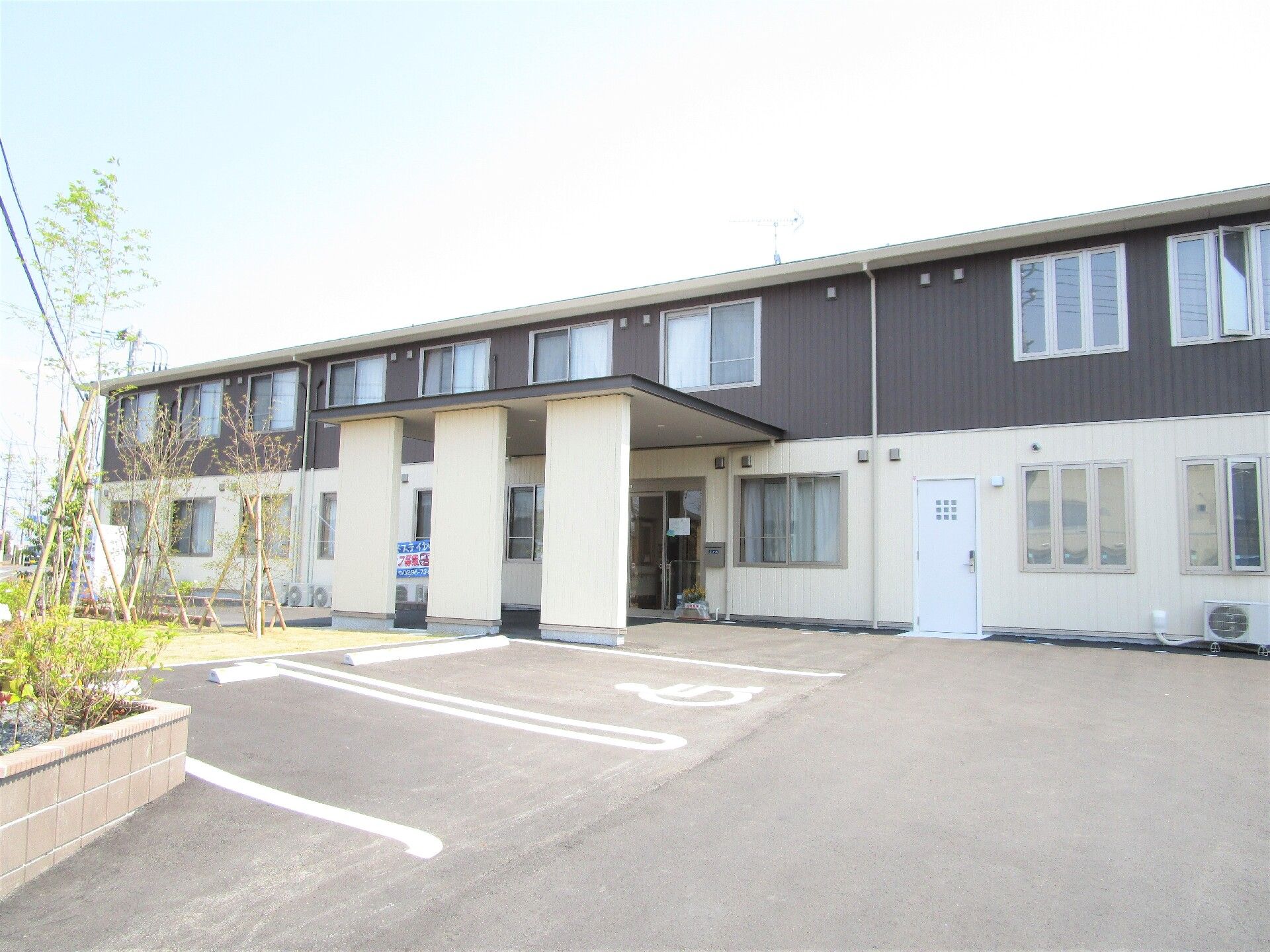 2階建ての建物。1階部分は白、2階部分はダークグレーで、広い駐車場もある。