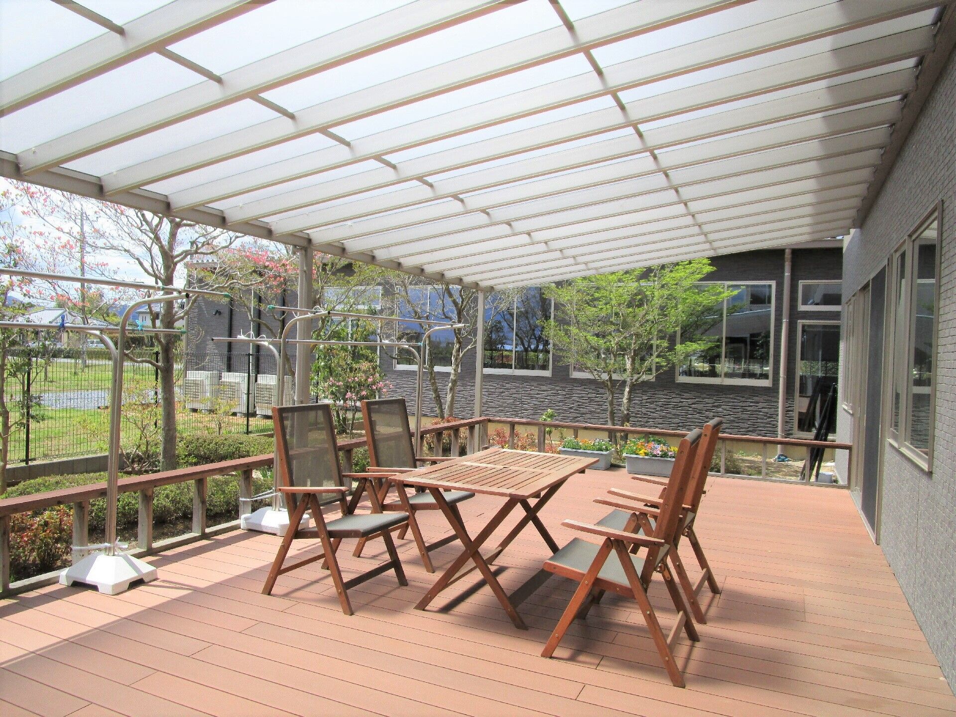 勾配の付いた半透明の屋根が付き、木製のガーデンテーブルセットと物干しが置かれたウッドデッキ