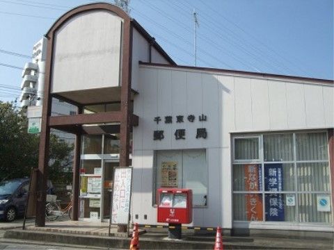 施設近隣にある郵便局の建物の外観である。建物は白色系で壁面には局名が表示され、入口は屋根付きになっている。