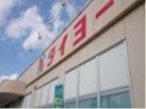 スーパーマーケットの店舗の外観である。建物の玄関には屋根が設置されており、壁面には赤字で店名が表示されている。