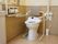 奥に便座付き便器が設置されている。トイレの両脇に手すりが、背後には背もたれがそれぞれ付いている。左側の壁には別種類の手すりが固定されている。
