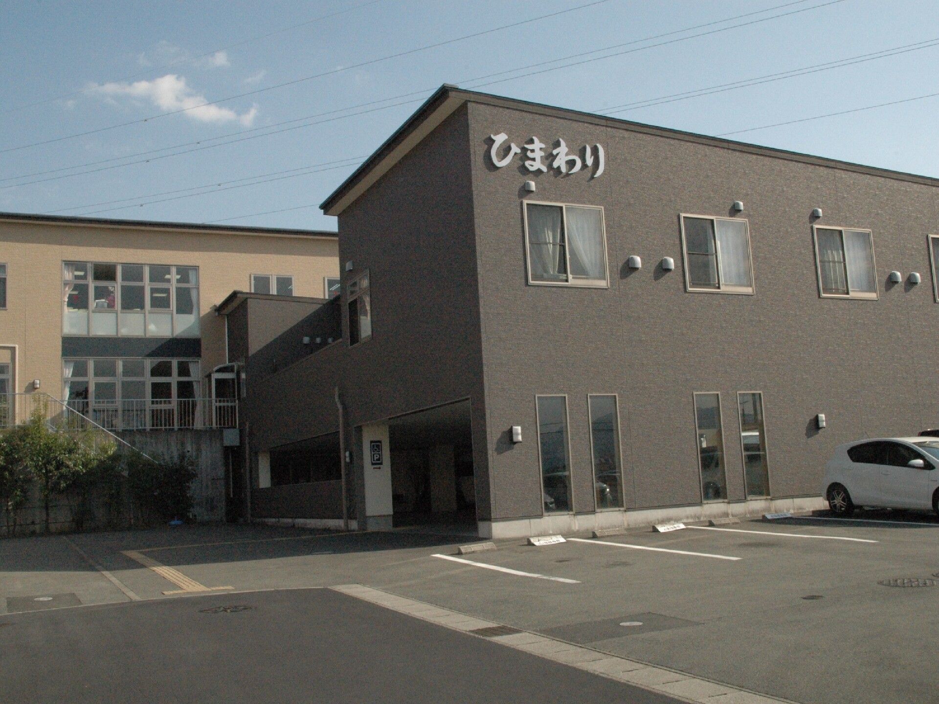 大きな駐車場が写っている施設の外観写真。シックな色合いの建物と広めの敷地内