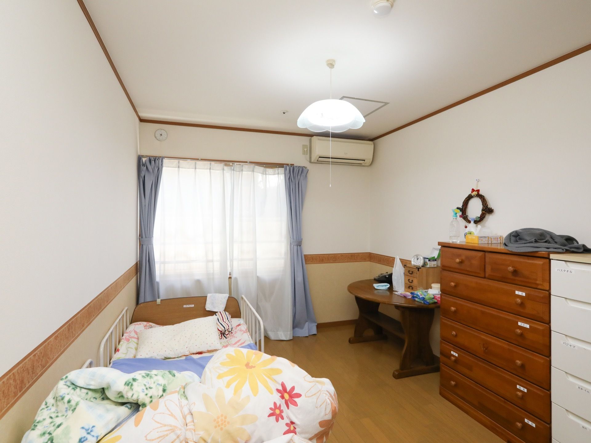 壁に窓やエアコンが設置された居室である。介護用ベッドが置かれ、入居者のお好みにレイアウトされている。