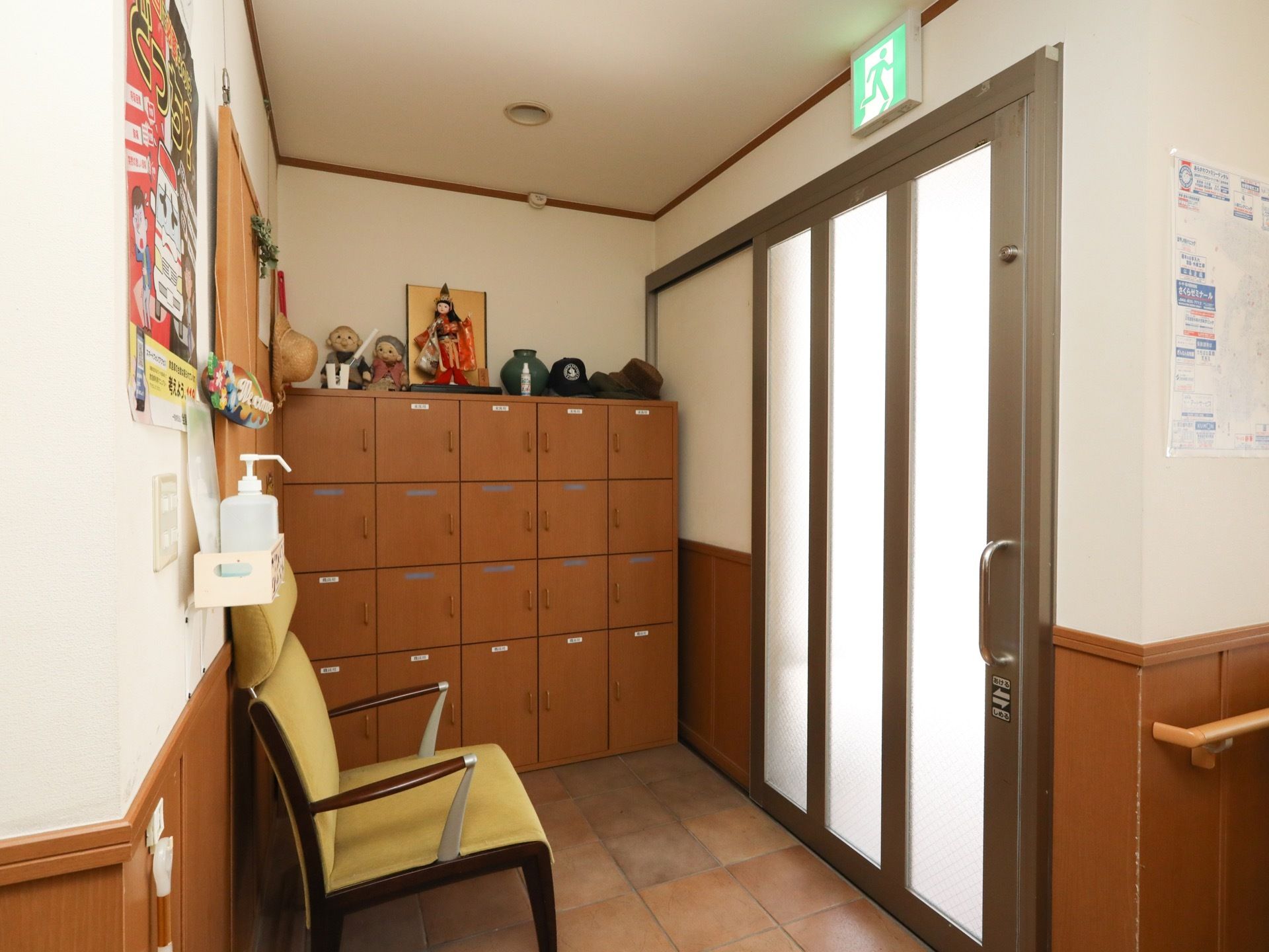間口広くスライド扉が設置された玄関には、非常口誘導灯が設けられている。靴収納のそばには、椅子が配備されている。