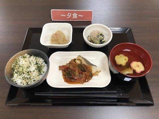 眼鏡をかけた車いすの男性入居者と女性スタッフが屋外での散歩を楽しんでいる。