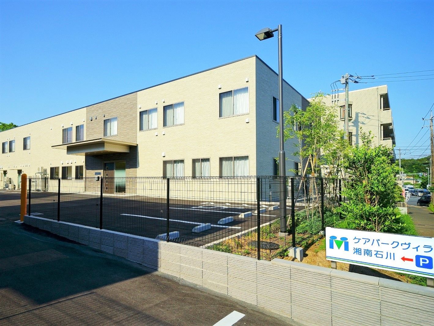 ２階建ての建物は敷地が広く、黒いフェンスで囲まれている。駐車場が付き、玄関には屋根がある。