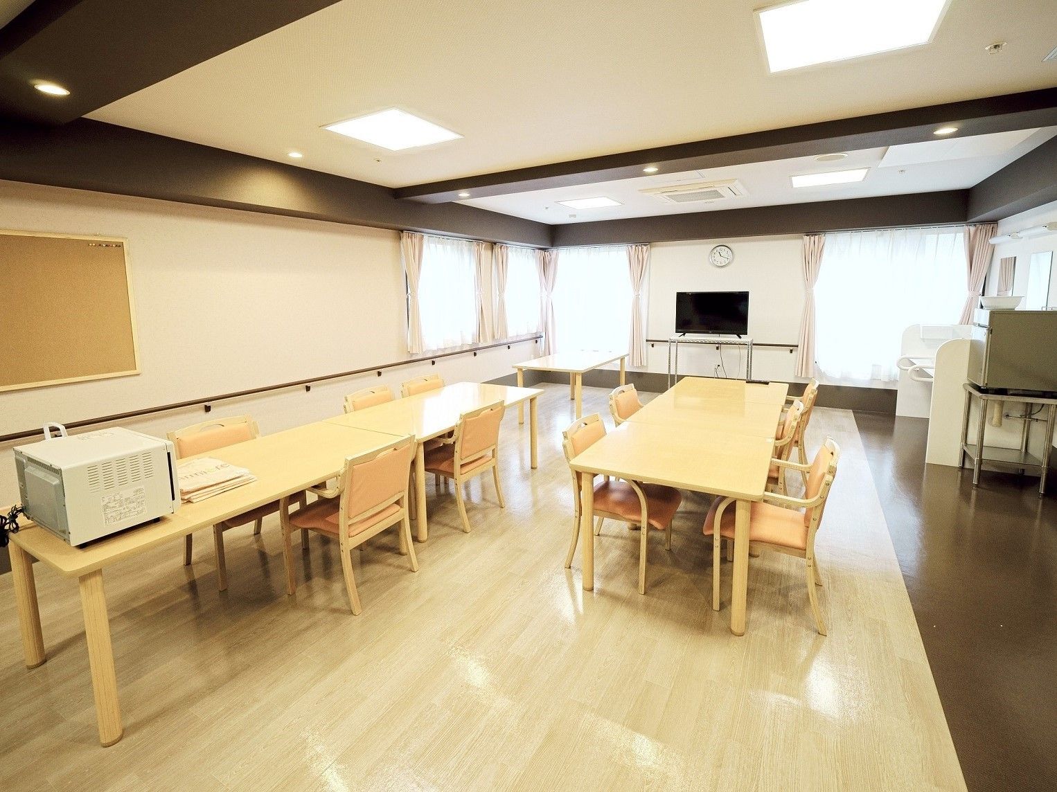 木製のダイニングテーブルが並んだ食堂の市場の句には大型テレビが置かれている。