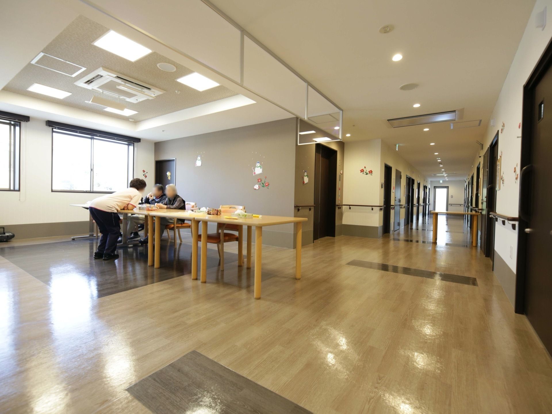 居室の廊下から通じる、談話用の共有スペースで、入居者様とスタッフが話をしている。壁がないので、居室からアクセスしやすい。