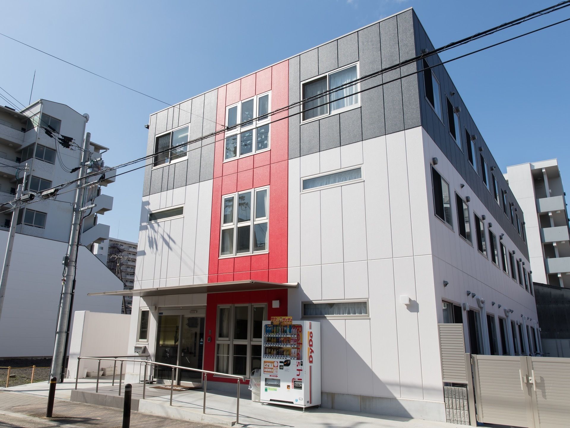 住宅街に溶け込む、モダンな３階建ての建物である。玄関前はなだらかなスロープになっており、自動販売機が設置されている。