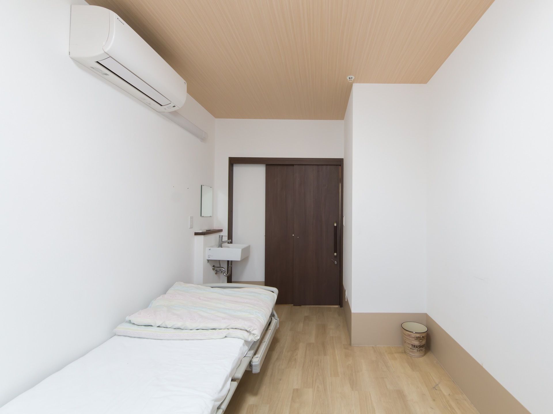 白と茶系でまとめられた、シンプルな個室タイプの居室である。ドアはスライド式で、電動ベッドのほか鏡付きの洗面台、エアコンが備え付けられている。