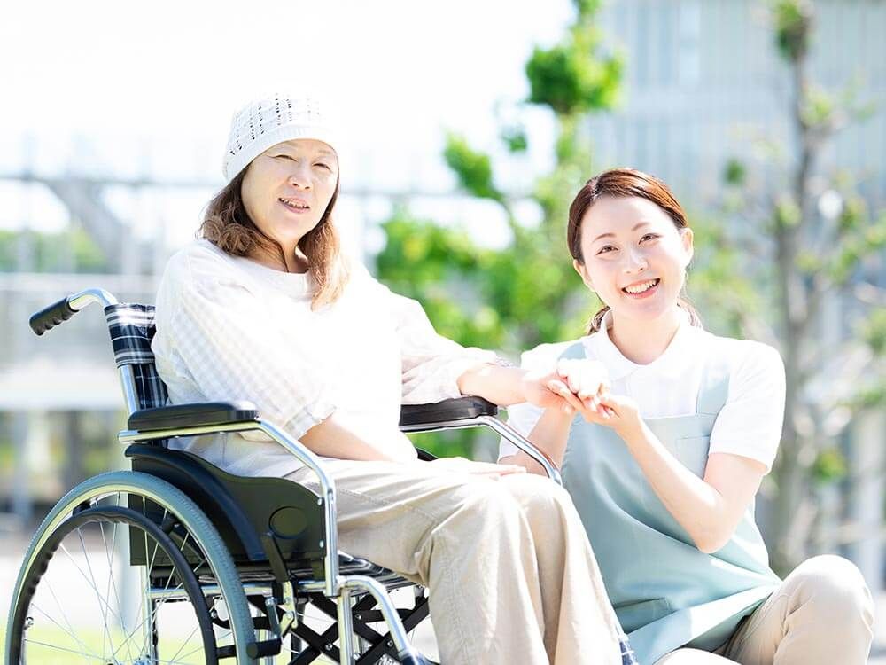 車椅子に乗った高齢女性と隣に寄り添う女性ヘルパー