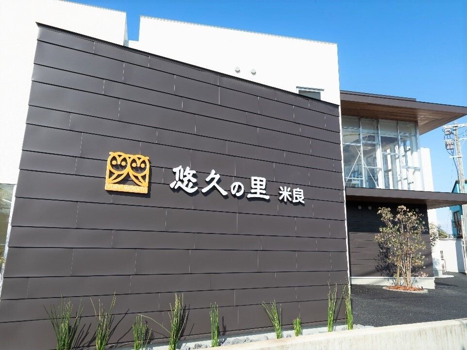 たくさんの木や花に囲まれた２階建ての建物は、ダークブラウンとグレー。