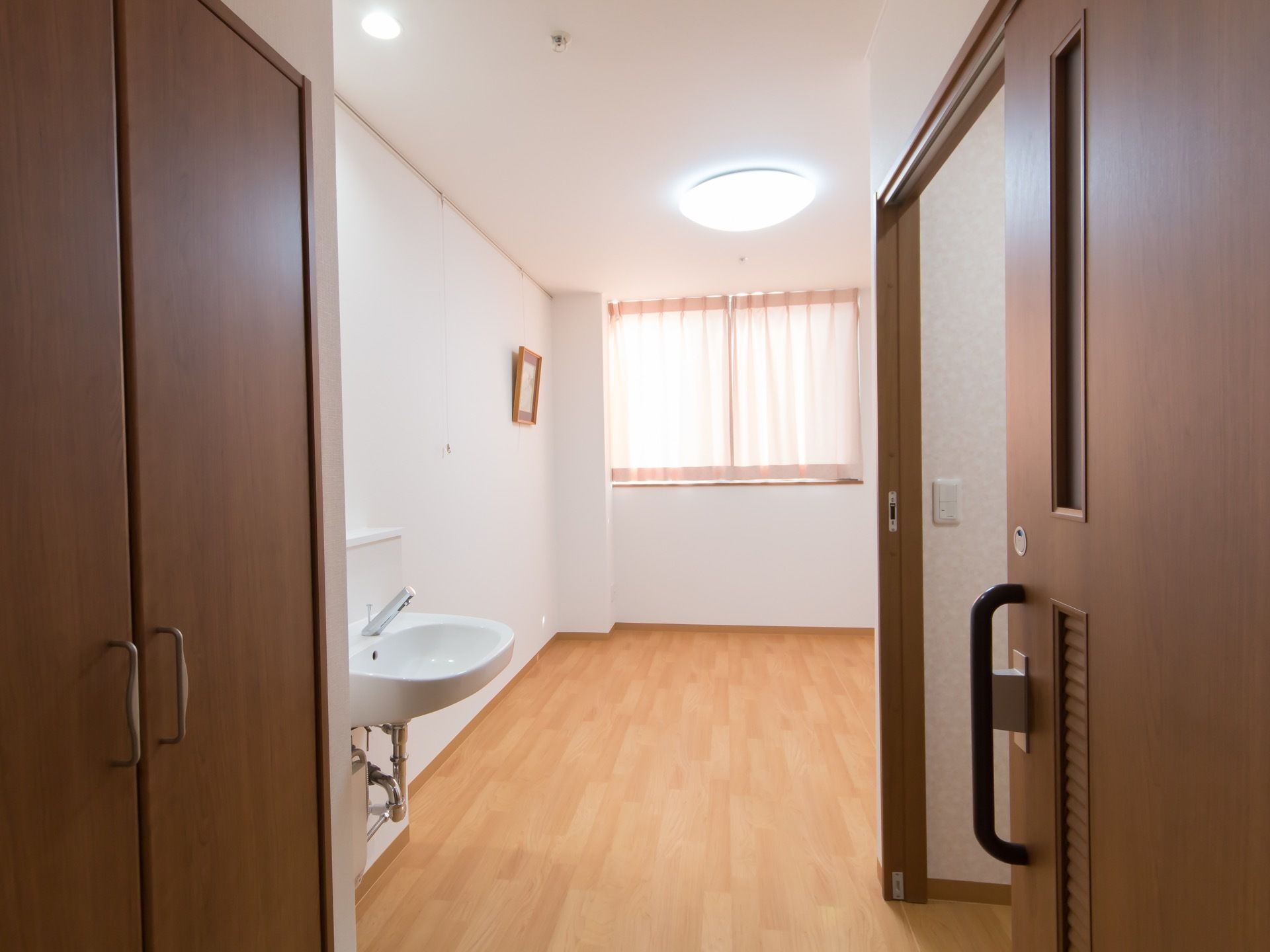 居室は白い壁と木のフローリングでナチュラルな印象である。建具も木調でまとめられている。天井に複数の照明、窓からの採光もあって明るい。